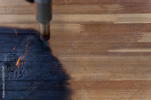 Obraz na plátne Gas torch burning the edge of a wooden surface, creating a black charred area with visible grain and small flames outdoors