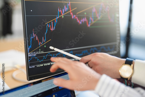 A person analyzes financial charts on a computer screen, using a stylus to point at the data.