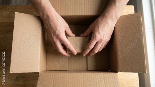 Hands placing item into box from top view, minimal hand visibility, ultra realistic commercial stock photography, 8k high resolution quality.