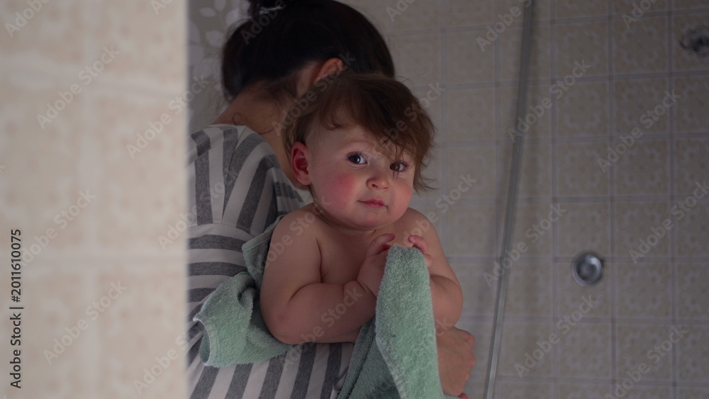 Fototapeta premium Baby chewing on towel while resting in mother’s arms after bath, intimate parenting moment of childhood curiosity, comfort, and gentle care at home