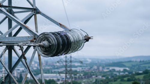 Global Infrastructure, Glass insulator string on high voltage transmission tower with electric arc and industrial landscape in background