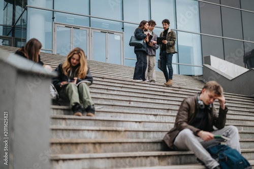 Fotografi A group of high school students converse and check a tablet while standing on outdoor steps