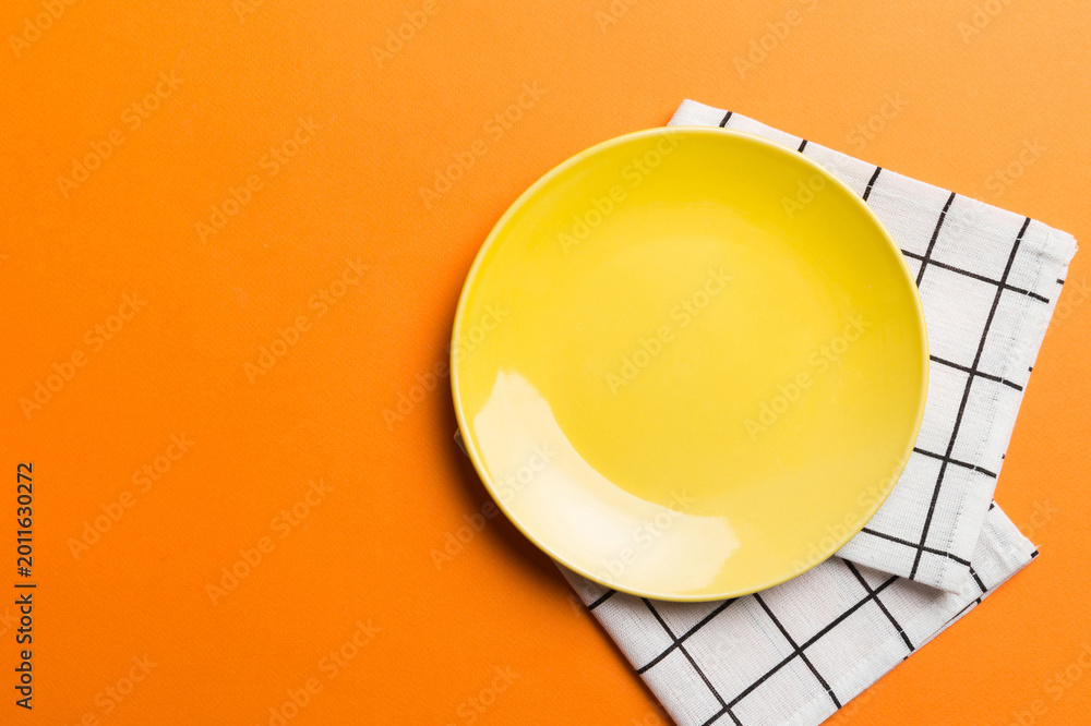 Fototapeta premium Top view on colored background empty round yellow plate on tablecloth for food. Empty dish on napkin with space for your design