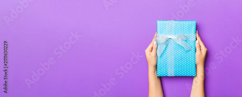 Cuadro en lienzo Flat lay of woman hands holding gift wrapped and decorated with bow on purple background with copy space