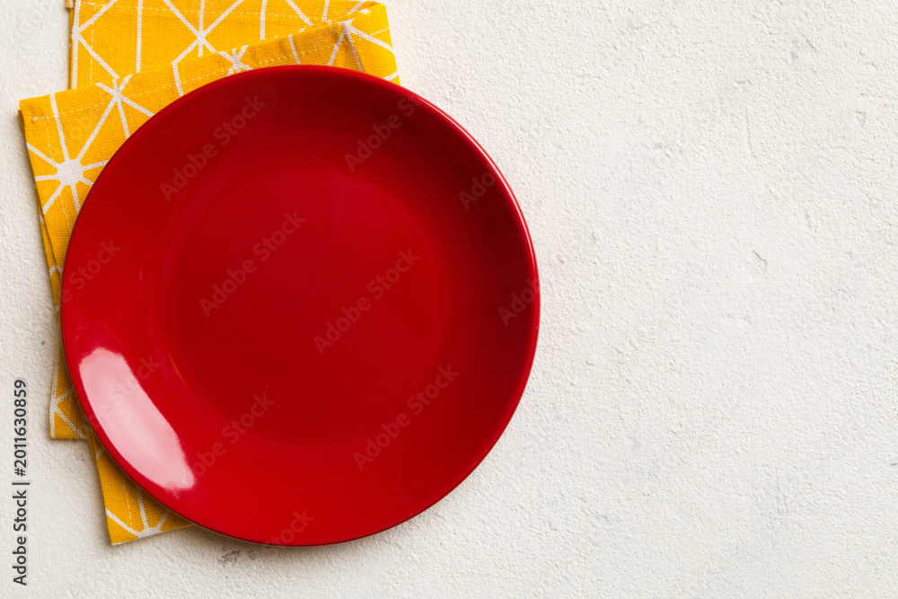 Fototapeta premium Top view on colored background empty round red plate on tablecloth for food. Empty dish on napkin with space for your design