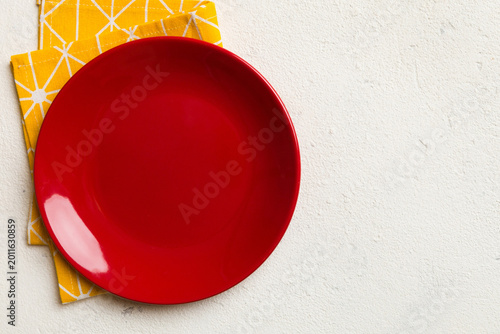 Top view on colored background empty round red plate on tablecloth for food. Empty dish on napkin with space for your design