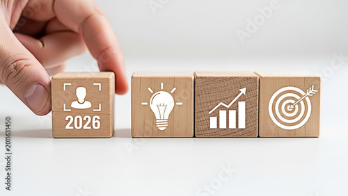 Hand placing a wooden block showing twenty twenty six with business growth and target icons