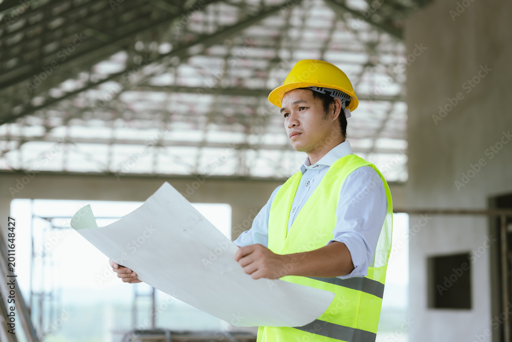Fototapeta premium Engineer in safety gear reviewing blueprints at a construction site, representing architecture, project planning, site inspection, and modern construction management.