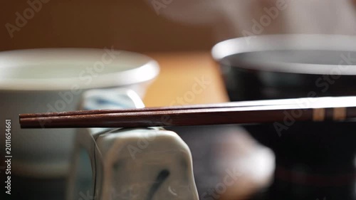 Japanese dining set with chopsticks resting on a ceramic holder, steam rising from bowls in a cozy, traditional atmosphere