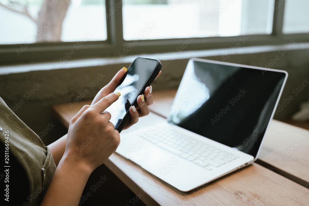 Fototapeta premium Close-up of a woman typing on a laptop at a wooden table in a cozy cafe, representing remote work, freelance lifestyle, online business, and modern digital communication.