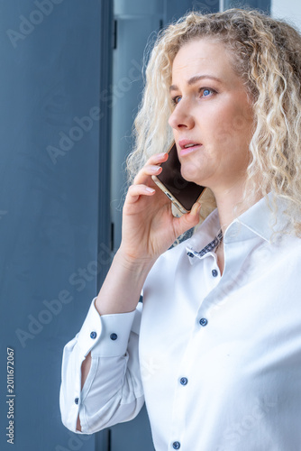 Serious businesswoman talking on phone by window, portrait, professional corporate communication concept, copy space banner

