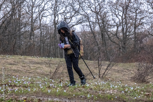 Photos Teenage girl in rain jacket with hood picks flowers on forest meadow during heavy rain