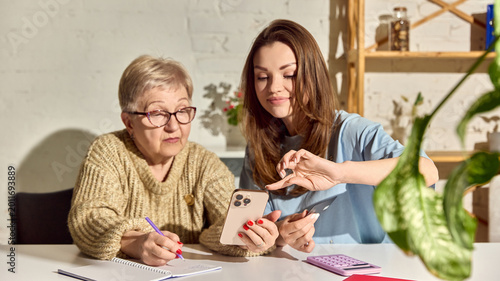 Foto Woman helping senior mother with mobile money transfer at home