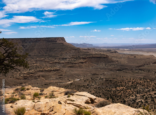 Принти на полотні Expansive desert canyon landscape with layered mesas, rocky foreground, and blue sky with clouds over a vast arid valley