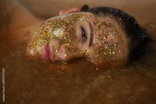 Φωτογραφία Portrait of a beautiful dark-haired young girl in golden water with a gold glitt