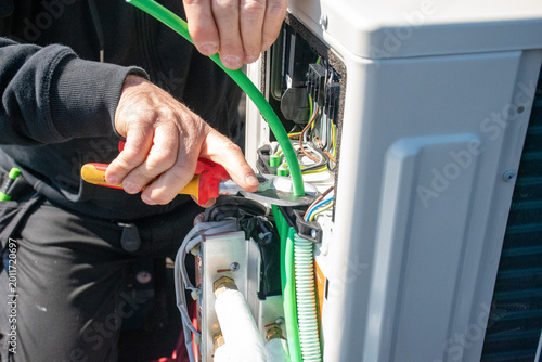 Technician Installing Modern Outdoor Air Conditioning Unit,Technician Working on an Air Source Heat Pump System,Close-up of Handyman Fixing Electrical Wiring in Outdoor Device