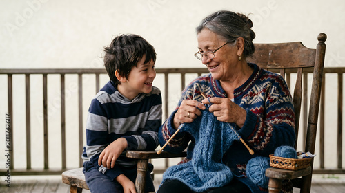 Russian grandmother and grandson bonding while knitting blue scarf on wooden chair outdoors