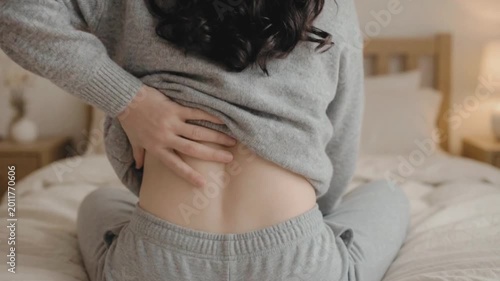 A woman in her thirties rubbing lower back to ease spinal pain and discomfort at home