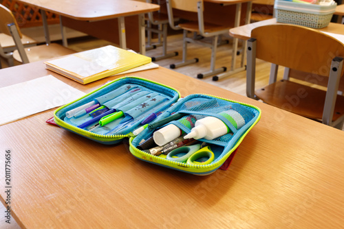 Open pencil case with school supplies on wooden desk in classroom. Pens, pencils, scissors and stationery on table. Back to school concept, elementary education, learning process, student workspace