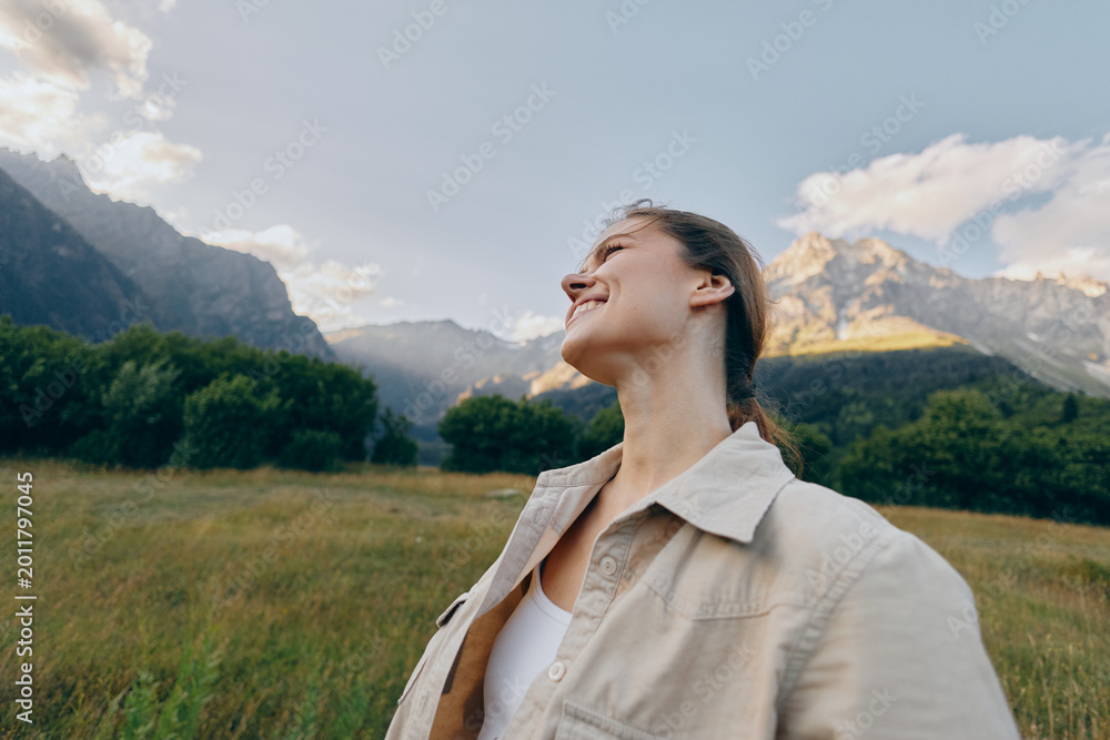 Fototapeta premium Vibrant outdoor portrait of a woman in a field enjoying nature and mountain views, a carefree mood and smiling expression, capturing lifestyle in a serene moment