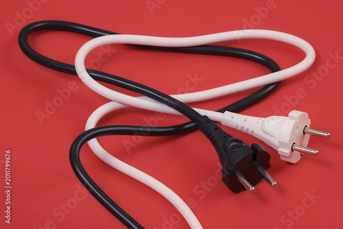 Black and white electrical power cables with plugs on a red background, representing household electrical usage.