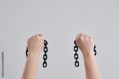 фотографія Female hands holding a broken metal chain over grey background with copy space