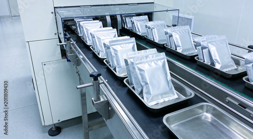 Automated packaging line processing silver pouches on a conveyor belt in a clean room