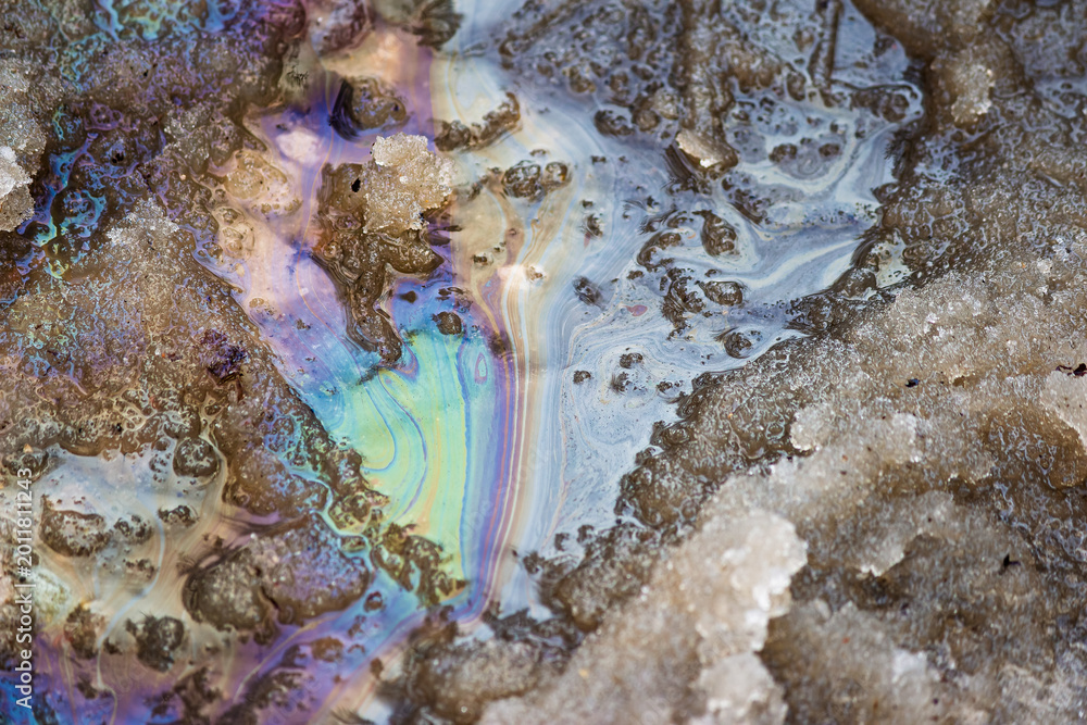 Fototapeta premium Iridescent oil slick on wet spring snow, showing colorful patterns from petroleum contamination in melting ice and water