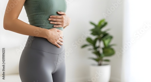 Young woman in activewear touches her stomach while feeling abdominal pain or digestive health issues