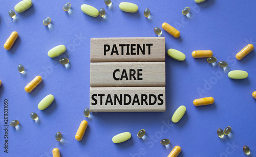 PATIENT CARE STANDARDS symbol. Concept words PATIENT CARE STANDARDS on wooden blocks. Beautiful purple background with pills. Healthcare and PATIENT CARE STANDARDS concept. Copy space.