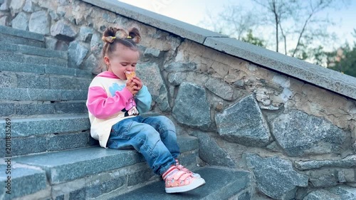 Child with an ice cream cone sitting on city steps during a summer walk. Cozy childhood atmosphere, leisure, and urban lifestyle concept