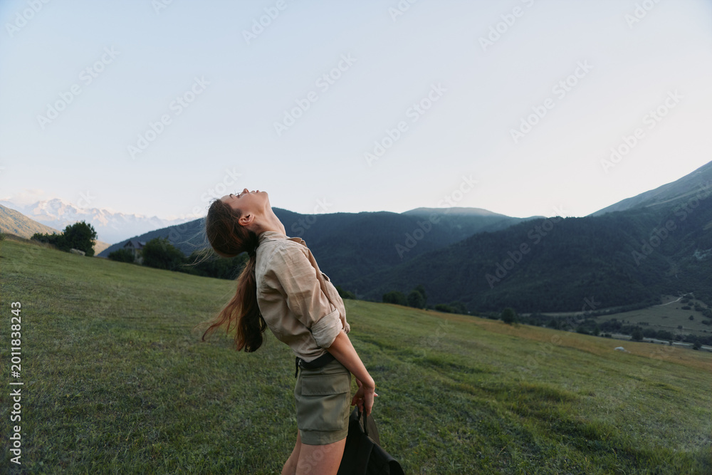 Naklejka premium Cheerful woman lifestyle outdoor countryside portrait casual, nature, sunshine, mountains and meadow, relaxed pose, sunlit breeze, blue sky, authentic candid moment in nature