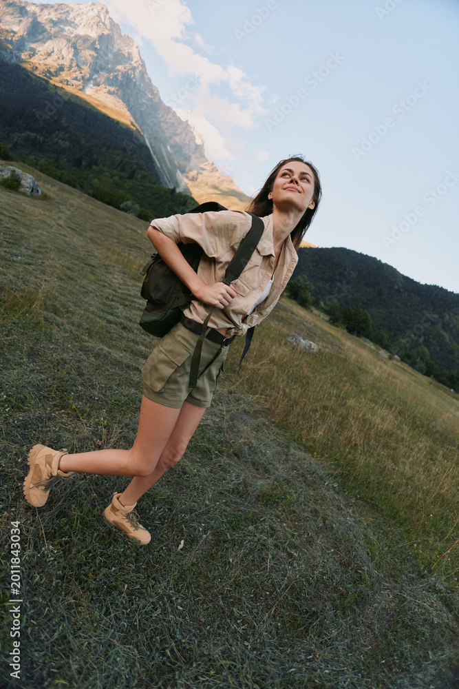 Naklejka premium A woman on a sunny hillside enjoys hiking, outdoors, and travel with a backpack, embodying adventure in a vast mountain landscape, clear sky, and peaceful nature.