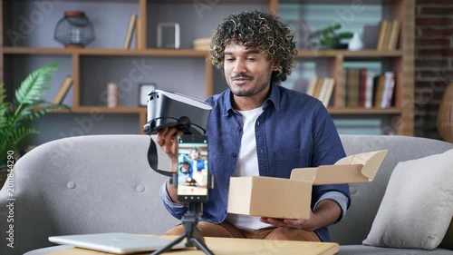 Male vlogger or blogger recording video blog while unboxing new modern VR headset in home office. Influencer conducts live streaming by phone leaving review about product giving feedback and advice