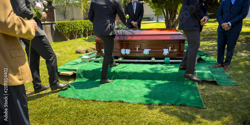 Фотография A group of men in suits walking by a casket with flowers and pallbearer gloves a