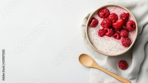 Bowl of yogurt with fresh raspberries and a wooden spoon on a white background captured in the kitchen during the day