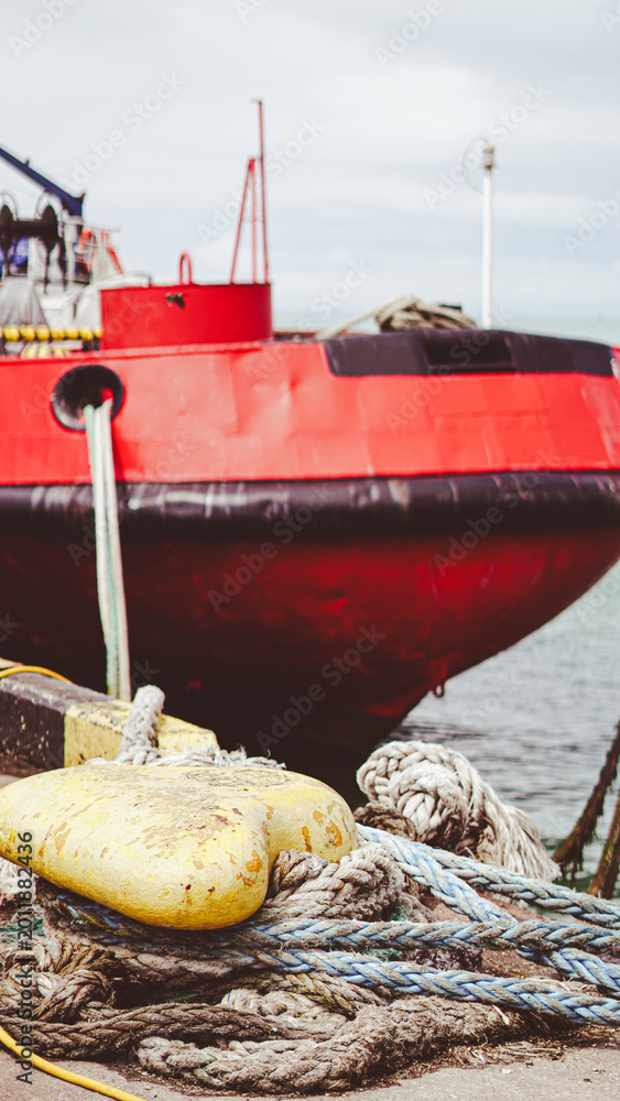 Fototapeta premium weathered mooring ropes and knots on a pier, with a large red industrial ship docked in the background