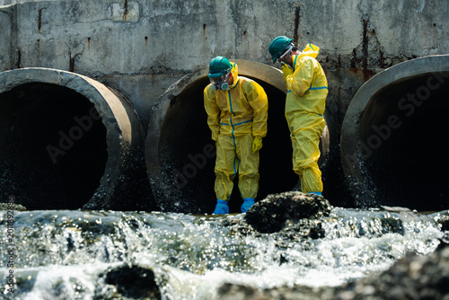 Hazmat workers in protective suits inspecting polluted wastewater drainage tunnel and contaminated industrial water during environmental hazard response operation