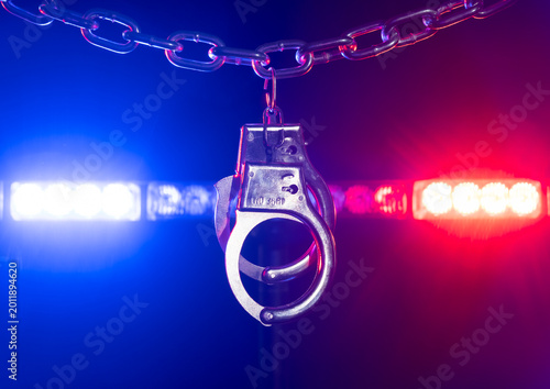 Police handcuffs hanging on a chain with red and blue lights flashing in the background during night hours in a law enforcement setting
