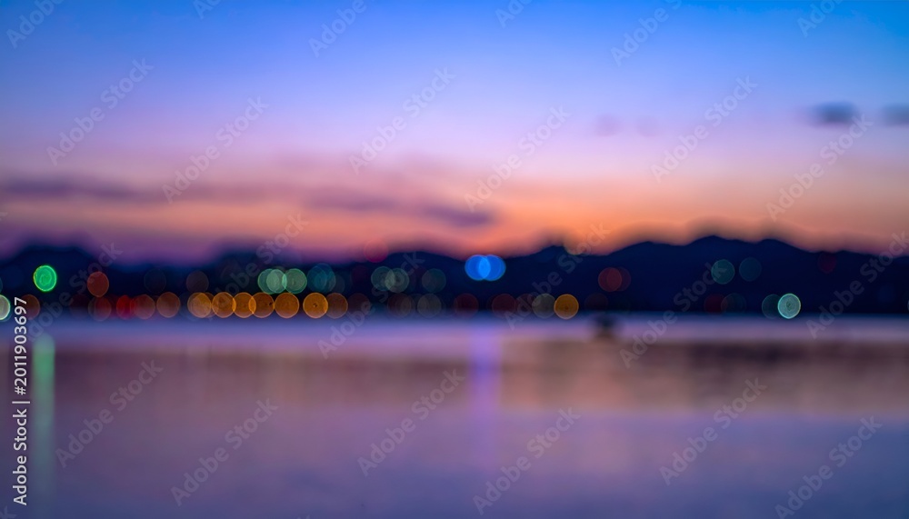 Fototapeta premium Blurred waterscape at dusk with bokeh lights reflecting on calm surface