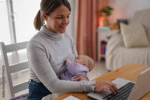Mother working with laptop in home office while breastfeeding newborn baby son - Motherhood, business and remote job concept