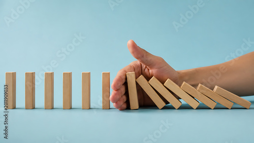 Business risk prevention concept with hand stopping falling wooden domino blocks symbolizing protection strategy crisis management and financial security