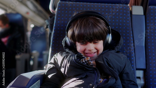 Fotografia Boy listening to music with headphones on train seat, happily reacting with exci