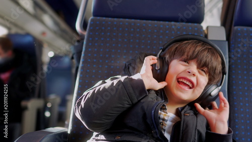 Slika na platnu Boy listening to music with headphones on train seat, happily reacting with exci