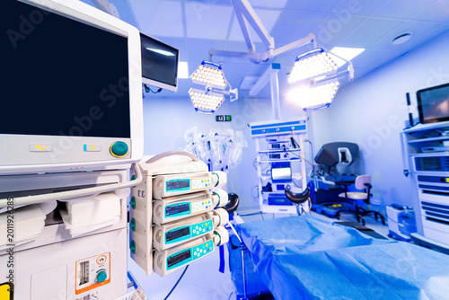 Infusion pump system and monitors in blurred operating room. Close up of medical dosing pumps and monitors with a surgical theater background in soft blue light.