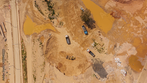 Aerial view discovering a construction site with heavy machinery including an excavator and dump trucks moving soil, creating new infrastructure and preparing the ground for future development