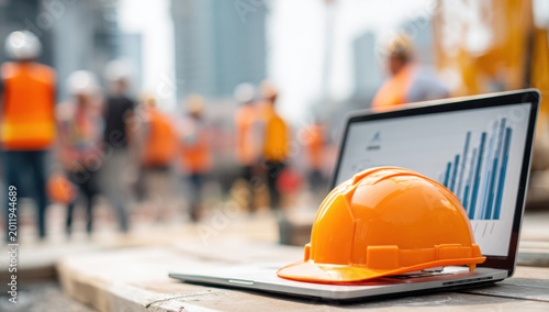 Construction project management with hard hat and laptop displaying data analysis chart on building site