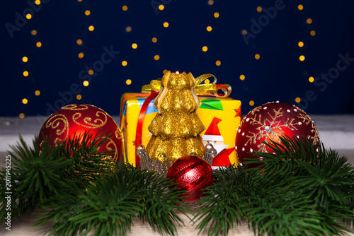 Between two large balls there is a Christmas tree in a stand and a small ball with a gift