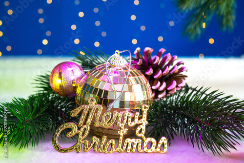 A golden ball with letters near Christmas tree branches with a small ball and a pine cone