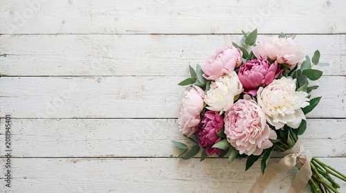 Beautiful bouquet of fresh pink and white peony flowers arranged elegantly on a rustic white wooden background perfect for wedding invitations and greeting card designs
